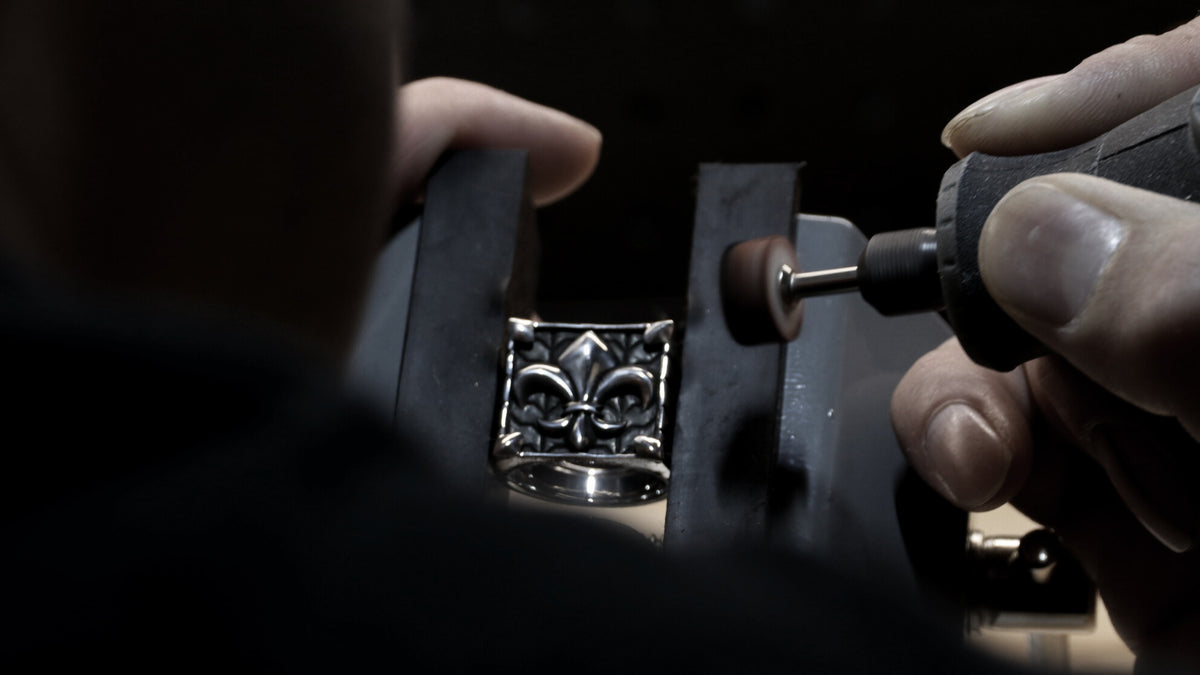 Person using a tool on a silver ring with a fleur-de-lis design.