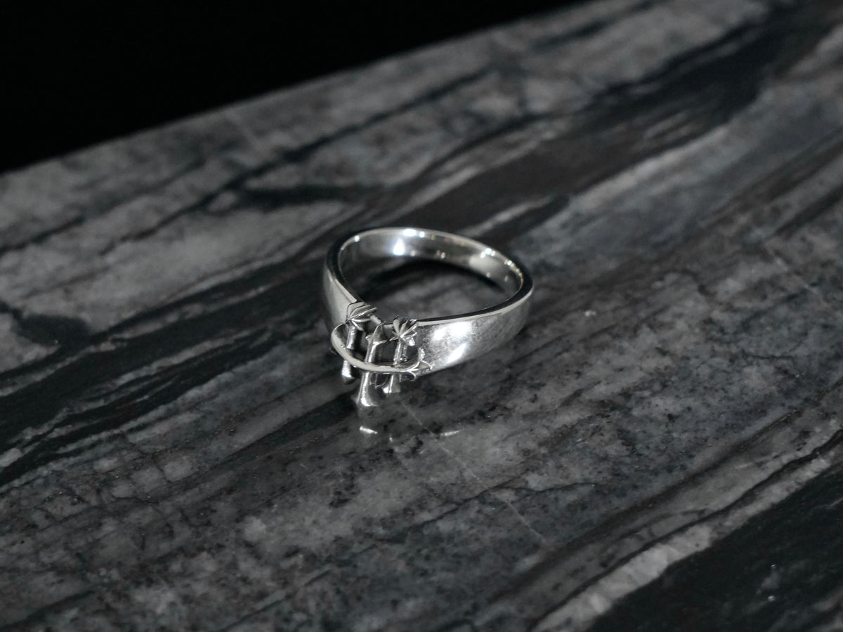 A sterling silver ring with the Rusbaron Troika symbol, resting on a dark, textured gray stone surface.