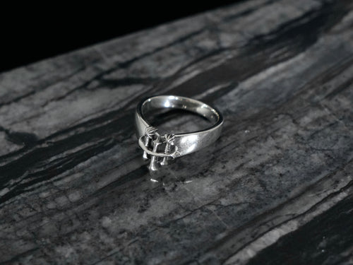 A sterling silver ring with the Rusbaron Troika symbol, resting on a dark, textured gray stone surface.