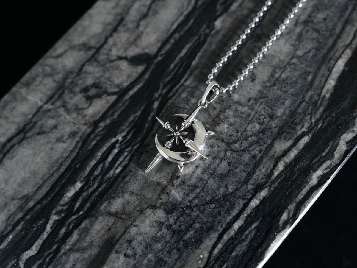 A silver-toned necklace with a starburst and crescent pendant, displayed on a dark gray and black marbled surface.