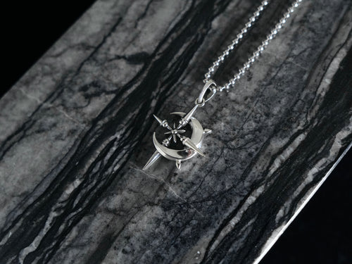 A silver-toned necklace with a starburst and crescent pendant, displayed on a dark gray and black marbled surface.