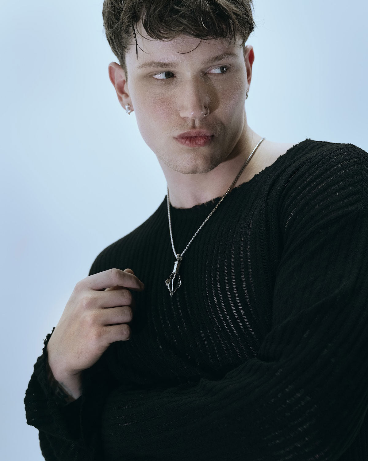 Man wearing a gothic mace-like silver pendant in a light blue background